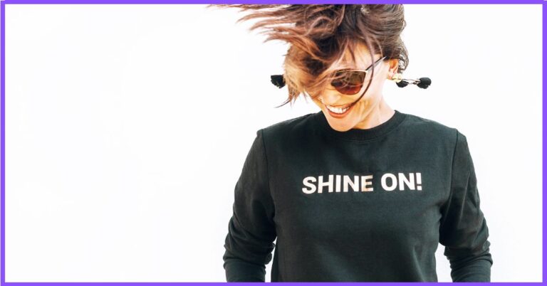 A person wearing a black sweatshirt with “SHINE ON!” written on it.