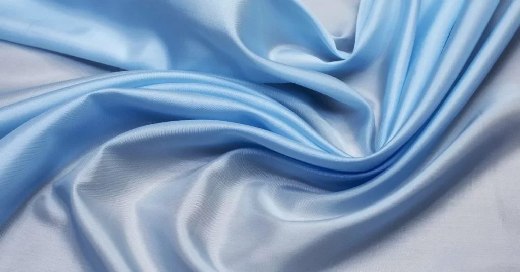 Close-up image of a smooth, light blue rayon fabric with gentle folds and creases showcasing its silky texture.