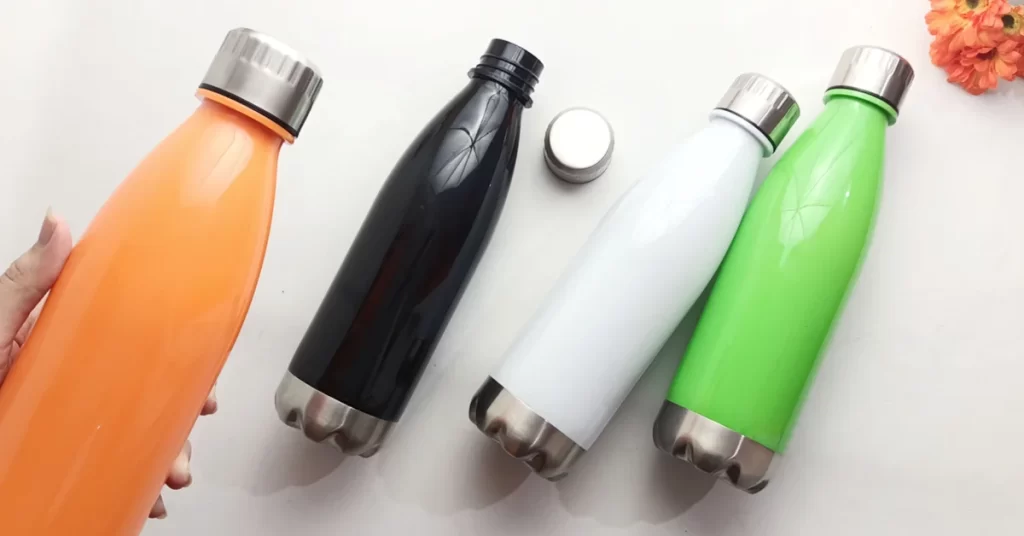 Water bottles in various colors (orange, black, white, mint green) with stainless steel bottoms and caps, displayed on a light background. The bottles are likely intended for sublimation printing as they have a matte finish suitable for the process.